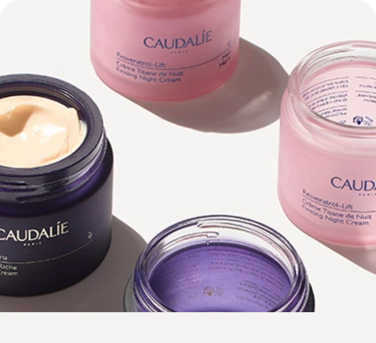 Open jars of Caudalie skincare creams in purple and pink containers, displayed on a white surface with shadows.